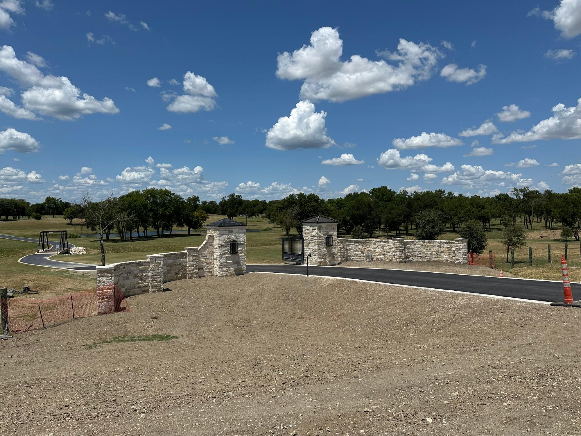 Limestone ranch entrance with gate columns, iron gate, and curved wing walls — masonry contractor, Temple TX
