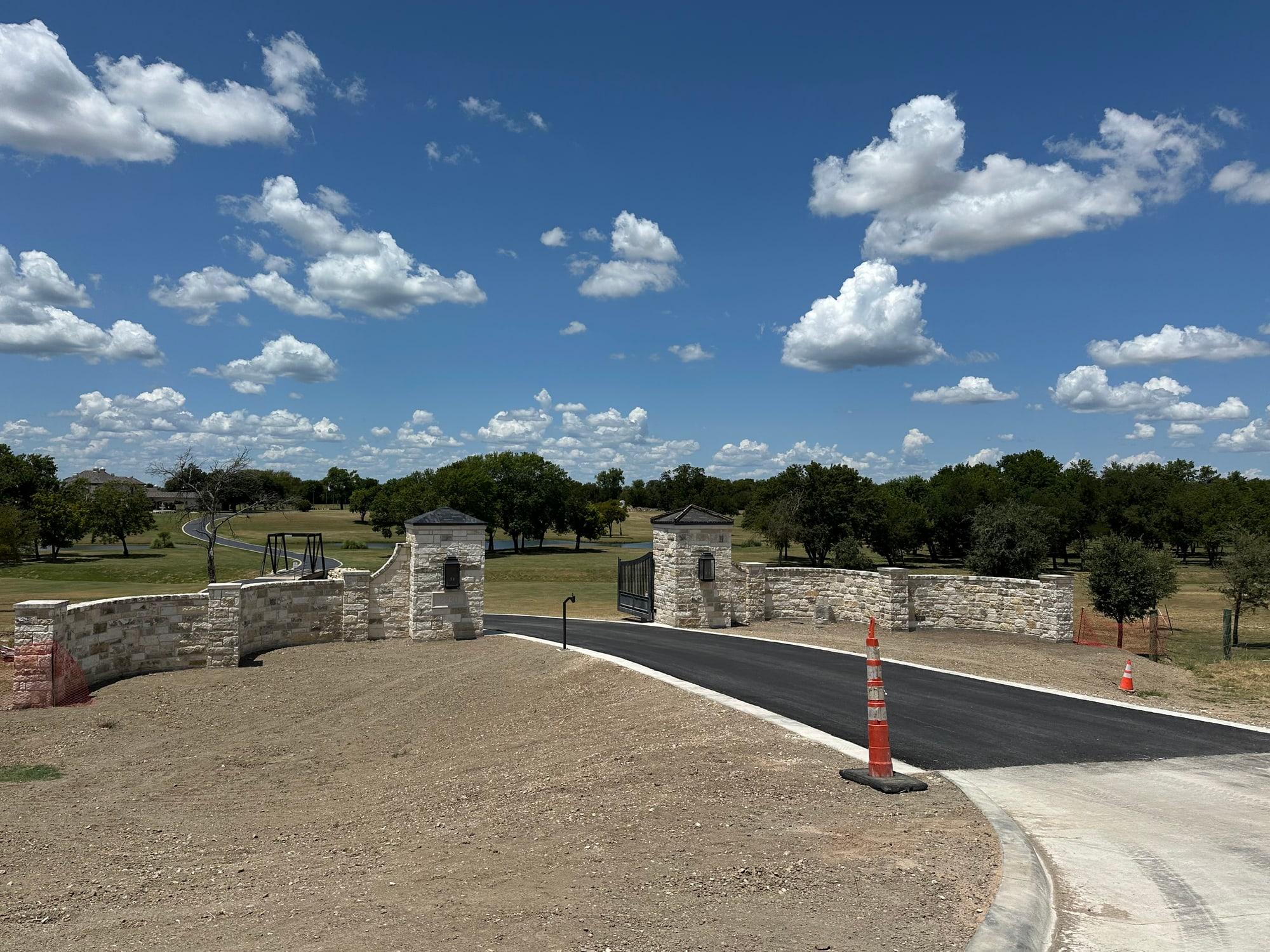 Ranch entrance columns and stone walls with the paved drive curving past the pond, Temple TX